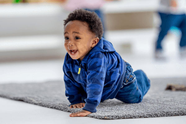 Smiling toddler crawling on gray carpet indoors