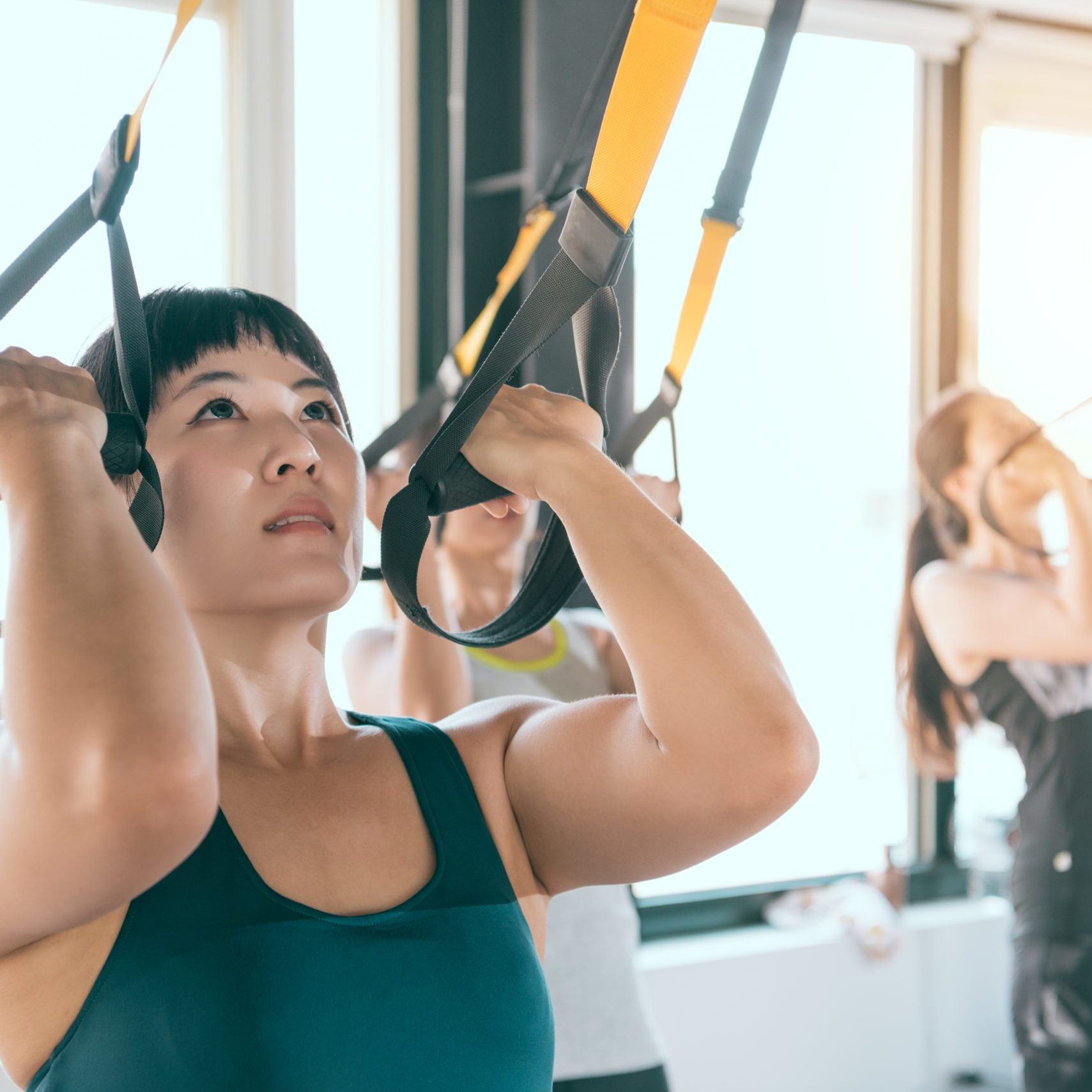 strong Asian woman using her muscle to pull up with her body training with TRX fitness system.