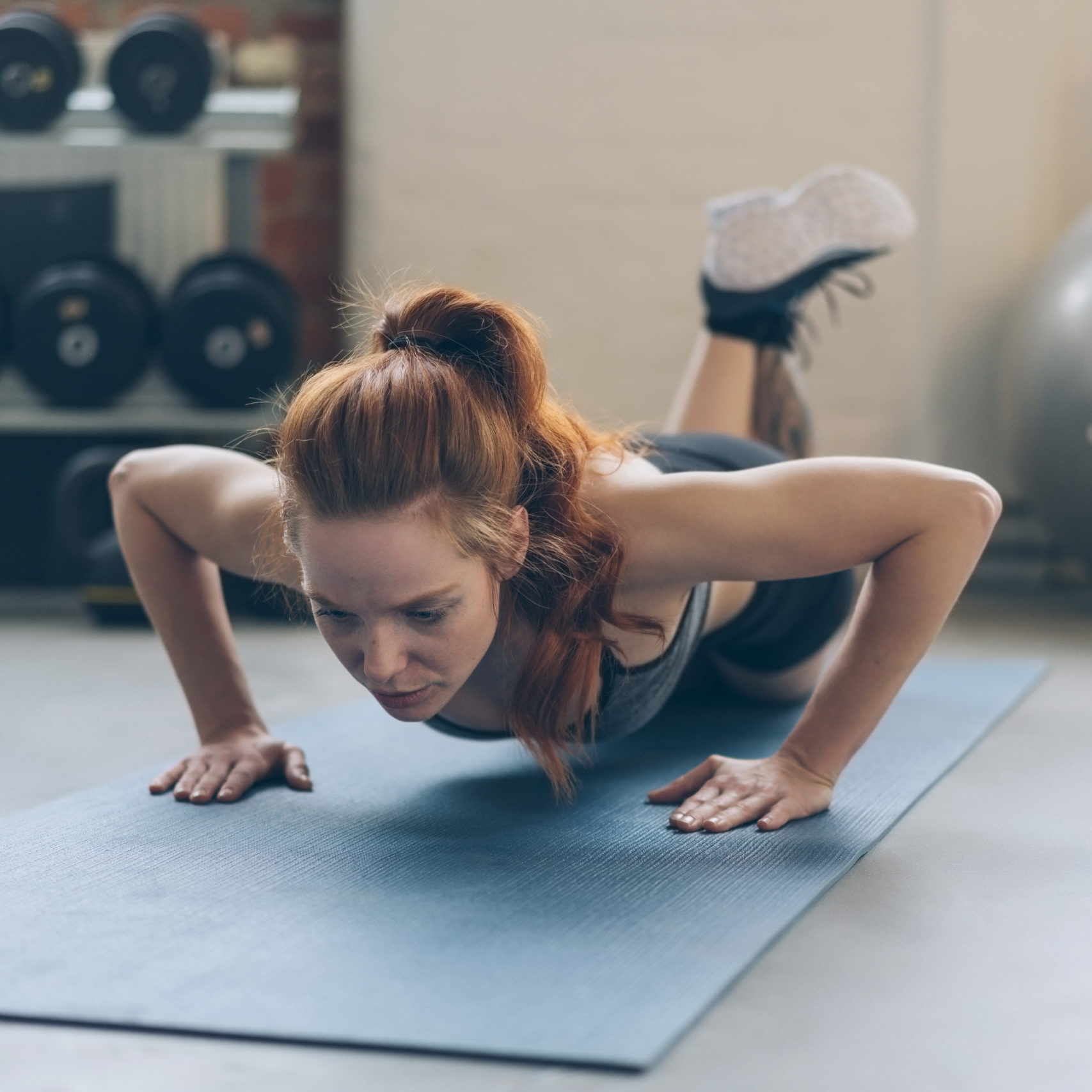 Fit young woman working out doing press ups on a yoga mat in a gym in a low angle view with gym equipment in the background