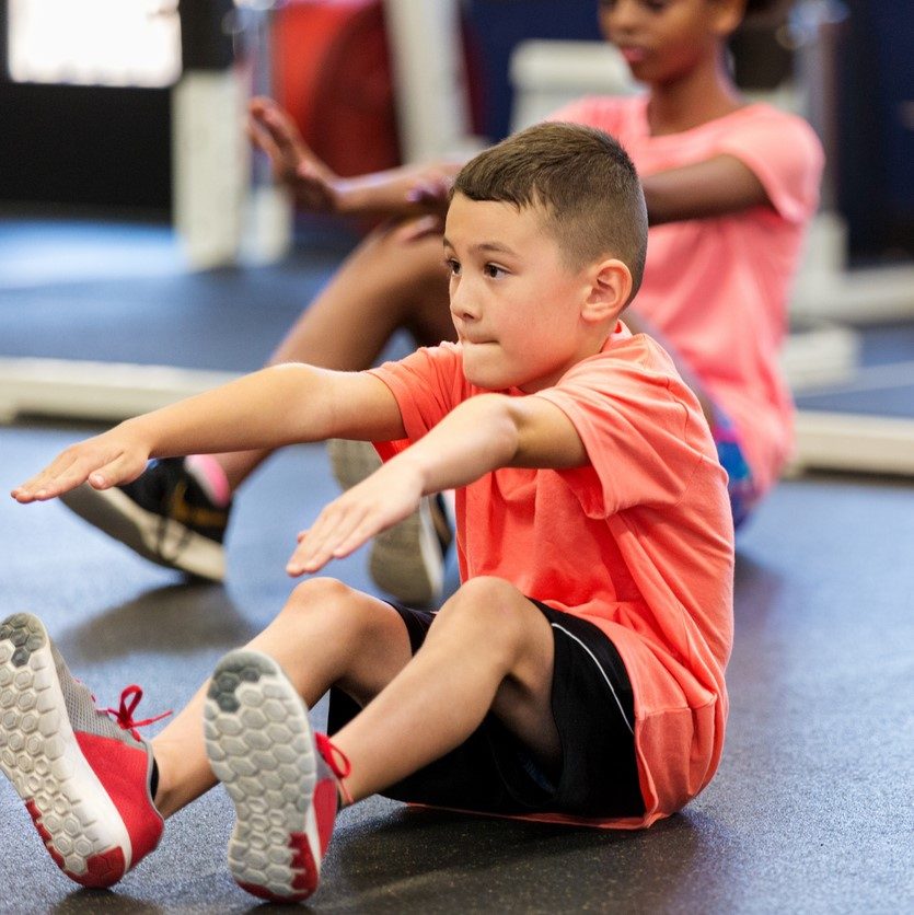 Elementary schoolboy concentrates while performing a sit up during fitness class or PE class.